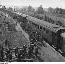 A black and white photo of numerous men, some carrying backpacks, heading for a train.