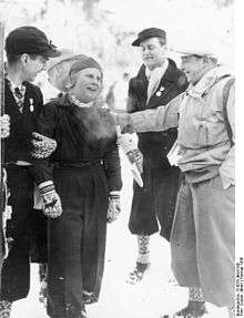 A Scandinavian woman is pictured standing surrounded by three men, one of whom is seen patting her shoulder.