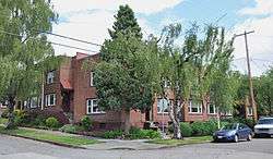 Photograph of a two-story, brick apartment building on a street corner