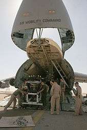 color photo of Marines pushing carted equipment from the open bay of a large cargo jet