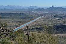 picture of a straight blue ribbon of water, the canal, running through the desert, from a vantage point of one of the mountains surrounding the city.