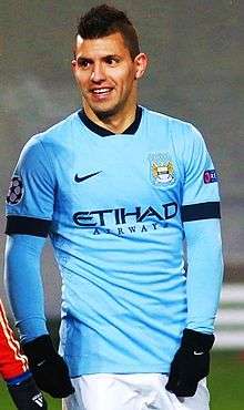 A man with wearing a sky blue long-sleeved football shirt with black Nike gloves.