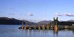 The ruins of an old building sit on top of a prominent hillock that overlooks a pier attended by fishing boats.