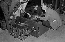 Four men in suits bend over a piece of machinery