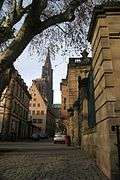 Gothic spire of a cathedral at the end of a street, taken from a cobbled square