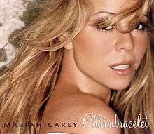 A blonde haired woman with her head looking towards the camera, on the bottom of the image, the words "Mariah Carey" and "Charmbracelet" are printed in front of a vector scroll art.