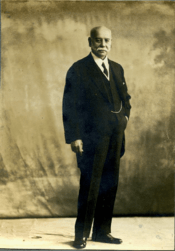 Full-length sepia portrait of distinguished gentleman with sideburns, wearing a 3-piece suit; body slight left-tilt