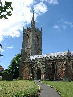 Stone building with square tower topped by a spirelet. The path in the foreground has grass on either side.