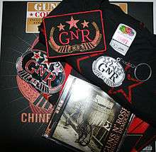 a patch with "GN'R" on it, a keychain, a shirt, a bandana, a sticker all with the same logo and a cd - items from the collector's edition of Chinese Democracy.