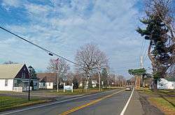 A two-lane road in a rural area with some mostly white wooden buildings along both sides