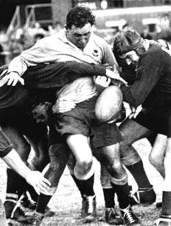 A rugby player attempting to break the tackles of two opposing players trying to restrain him