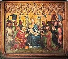 Rectangular central section of an altarpiece in the International Gothic style, showing the Three Kings adoring the Christ Child. The arrangement is formal, balanced and intricately detailed. The Virgin Mary, in a robe of brilliant blue sits enthroned with Jesus on her knee at the center of the painting. The figures have a sweet, doll-like quality. On either side kneel the two older kings clothed in robes of patterned velvet, one green and the other crimson, with gifts of a golden box and a silver chalice. The youngest king stands behind one of the kneeling figures, and presents a container of semi-precious stone.