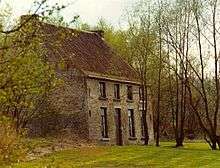 photo of a two-storey brick house on the left partially obscured by trees with a front lawn and with a row of trees on the right