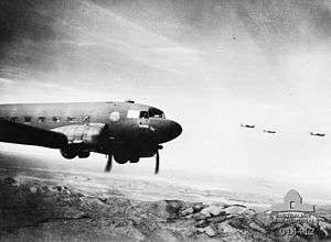 Four twin-propeller aircraft fly over a mountain range