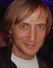 A close-up of a man with medium-length brown hair and hazel eyes looking straight ahead