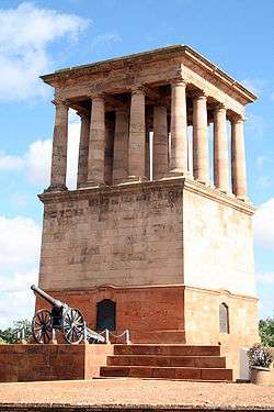 The Honoured Dead Memorial, a tall, brown sandstone building with multiple Grecian-type pillar and the Long Cecil gun at its base
