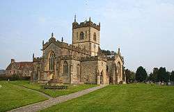 Yellow stone building with central square tower, Foreground is paths through green grass