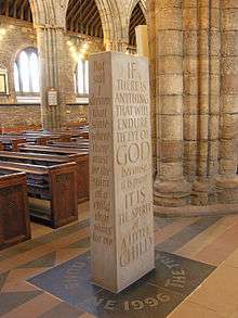 a cuboid-shaped standing stone with words engraved on its sides and on the floor where it stands.