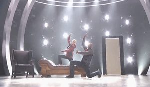 A screenshot showing an older Caucasian woman with her dance partner, a tall African-American male, on a shinny gray stage at the end of their hip-hop performance.