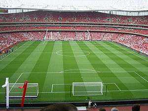 An interior view of a football stadium. There are no players on the pitch but there are spectators in the stands.