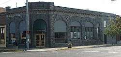 Photograph of a one-story, stone commercial building on a city street corner