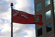 A red flag with the Union Jack in the top left corner and a coat of arms depicting a bison in the lower right corner flies beside a building