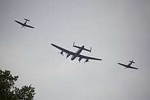 Rear view of a three-aircraft flypast. In the middle is a four-engine bomber, which is flanked on both sides by propeller-driven fighters