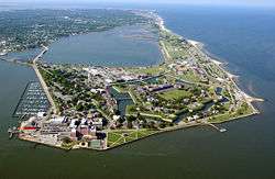 An aerial view of a flat promontory of land with a large fortification in the center. There are many modern buildings and roads surrounding the fort.  On either side of the promontory are wide expanses of water.