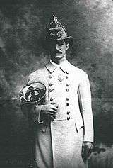 A man in a white coat and fire helmet holding a brass horn