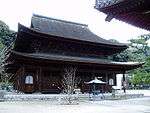 Large wooden building with a hip-and-gable roof and an enclosing pent roof.