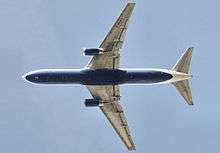 Underside view of a jet in-flight. Each wing of the two wings have an engine. Towards the left are the horizontal stabilizers.