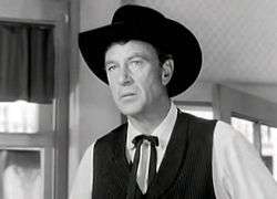 Man in dark vest, white shirt, dark cowboy hat, and western tie