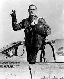 A man standing in the cockpit of an aircraft which is on the ground.