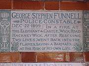 A tablet formed of two large tiles, bordered by green flowers in the style of the Arts and Crafts movement