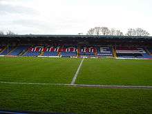 Bury's blue stadium seated stand covered in red, white and black F.C. United banners.