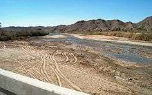 A shallow river with a sandy bed flows through an arid landscape.