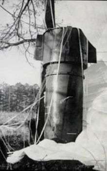 A big metallic cylinder standing upright in a field next to a tree