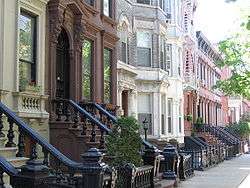 A view down a street with rowhouses in brown, white, and various shades of red.