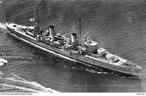 Three-quarter overhead view of cruiser with twin funnels and four gun turrets, at sea