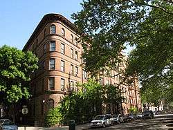 Brick townhouses along a street, which is lined with trees.