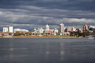 A city located on the opposite side of a large river, with a domed building in center of the city.