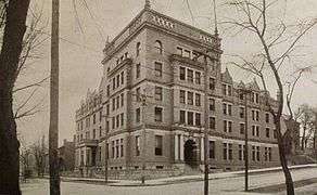 A 5 story stone building built on a street corner, with two entrances