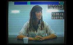 Old computer footage of a 37-year-old woman in a white shirt with long brown hair, sitting at a police interview desk. She is holding her hands together in front of her, and is looking to the right of the camera. There is a subtitle that reads "Please." At the top of th screen is a scroll bar, positioned at one-third.