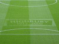 A photograph of a green football turf, with the words Highbury, 1913–2006 etched in the middle.