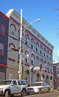 A three-story high brick building with a decorative facade mostly painted yellow photographed from its left. Two police cars and a streetlight are in front.