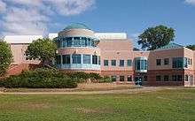 A beige building with a large windowed rotunda stands before a large lawn.