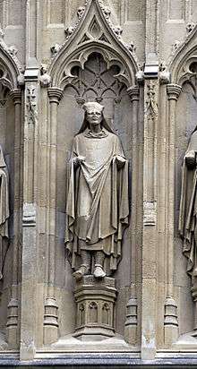 Stone statue of a robed man set in a niche. The top half of the head of the statue is missing.