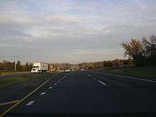 Eastbound IL 120 west of Hunt Club Road. Road is divided highway with a grassy median and open areas on both sides with scattered trees.