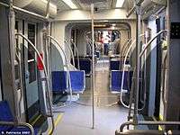 Interior of a light rail vehicle with blue seats, gray walls and silver pedestrian supports.