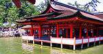 A wooden building with red beams on poles above water.